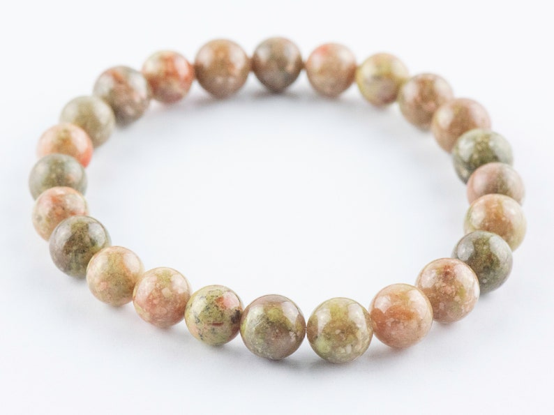 May include: A bracelet made of round, green, brown, and pink speckled beads.
