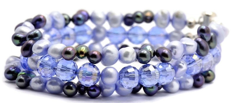 May include: A multi-strand bracelet featuring a combination of light blue and dark blue glass beads and iridescent white pearls.