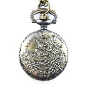 May include: A gold-toned pocket watch with an ornate floral design on the face. The watch has a silver-toned chain and a decorative loop.