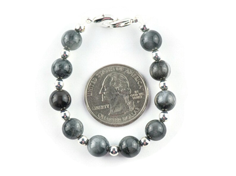 May include: A gray and silver beaded bracelet with a silver clasp. The bracelet is about the size of a US quarter.