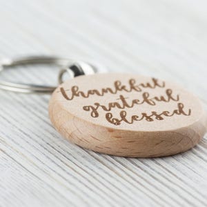May include: A wooden keychain with a round charm that says "thankful grateful blessed" in a cursive font.