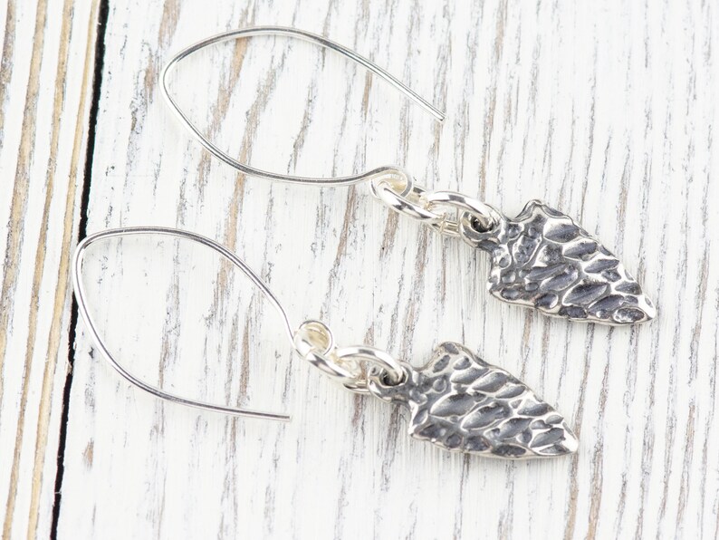 K&ouml;nnte beinhalten: Ein Paar silberne Ohrringe mit einem strukturierten Pfeilspitzen-Design. Die Ohrringe sind aus Sterlingsilber gefertigt und haben ein schlichtes, elegantes Design.