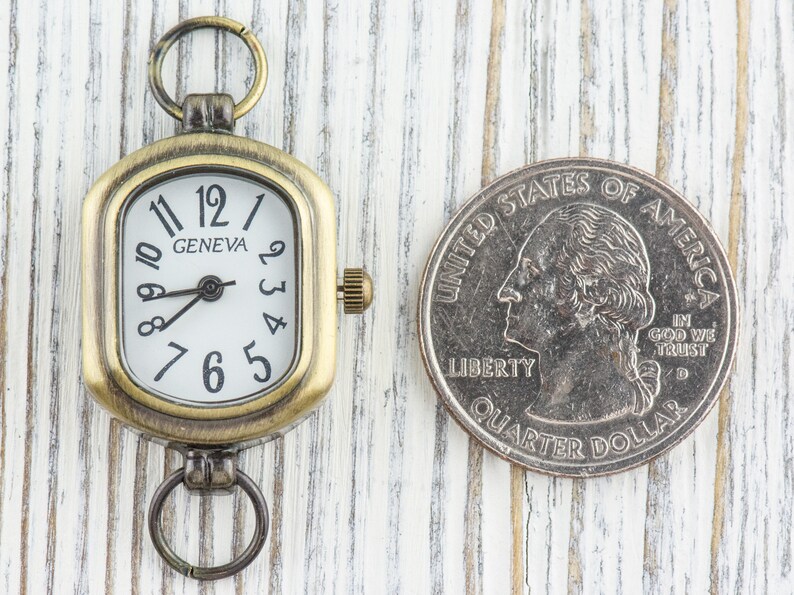 Pu&ograve; includere: Un piccolo orologio da tasca in stile antico con un quadrante quadrato e numeri romani. L'orologio ha una finitura in ottone e un quadrante bianco con lancette nere. L'orologio &egrave; appeso a una catena argentata.