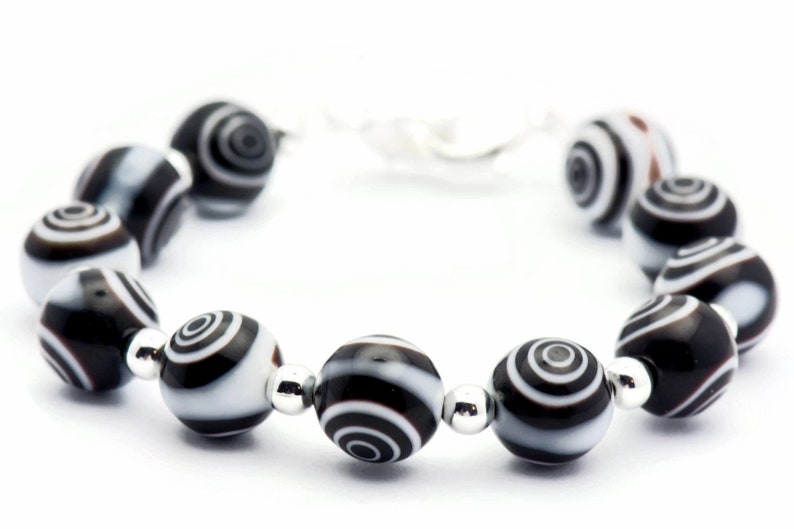 K&ouml;nnte beinhalten: Ein schwarz-wei&szlig;es Armband mit runden, gemusterten Perlen. Die Perlen haben ein wirbelndes, konzentrisches Kreisdesign.