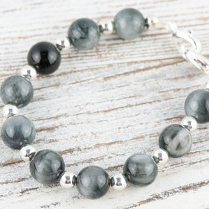 May include: A gray and black beaded bracelet with silver accents. The bracelet is made with round beads and a silver clasp.