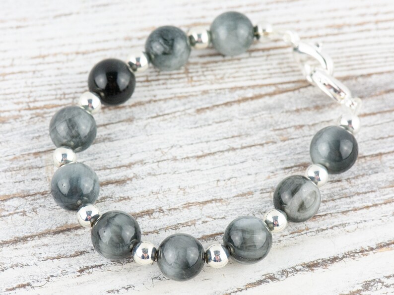 May include: A gray and black beaded bracelet with silver accents. The bracelet is made with round beads and a silver clasp.