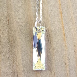 Pu&ograve; includere: Una collana con catena d'argento con un ciondolo di cristallo trasparente. Il ciondolo &egrave; rettangolare e ha un design sfaccettato.