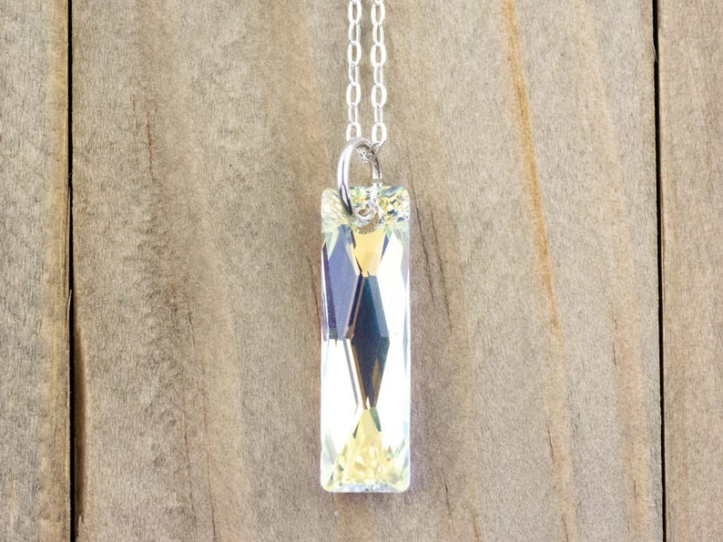 Pu&ograve; includere: Una collana con catena d'argento con un ciondolo di cristallo trasparente. Il ciondolo &egrave; rettangolare e ha un design sfaccettato.