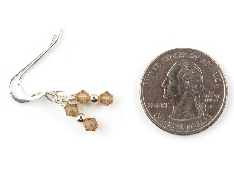 May include: Silver dangle earrings with a small cluster of brown crystal beads. The earrings are about the size of a UK 20 pence coin.