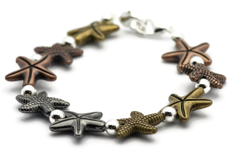 May include: A silver chain bracelet with multiple starfish charms in different colors, including copper, gold, and black.