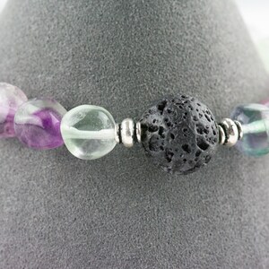 Puede incluir: Un brazalete hecho con cuentas de fluorita verde, p&uacute;rpura y blanca y una cuenta de roca de lava negra. El brazalete tiene cuentas espaciadoras plateadas.