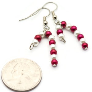 May include: A pair of silver dangle earrings with red and white beads, shaped like candy canes. The earrings are about the size of a quarter.