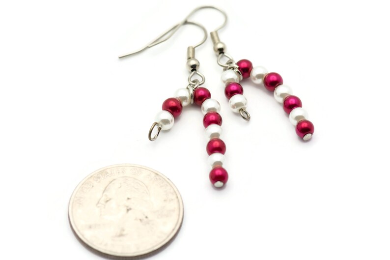 May include: A pair of silver dangle earrings with red and white beads, shaped like candy canes. The earrings are about the size of a quarter.