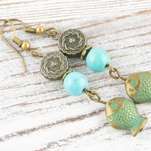 May include: A pair of turquoise and bronze earrings featuring a fish charm, turquoise beads, and ornate bronze accents.