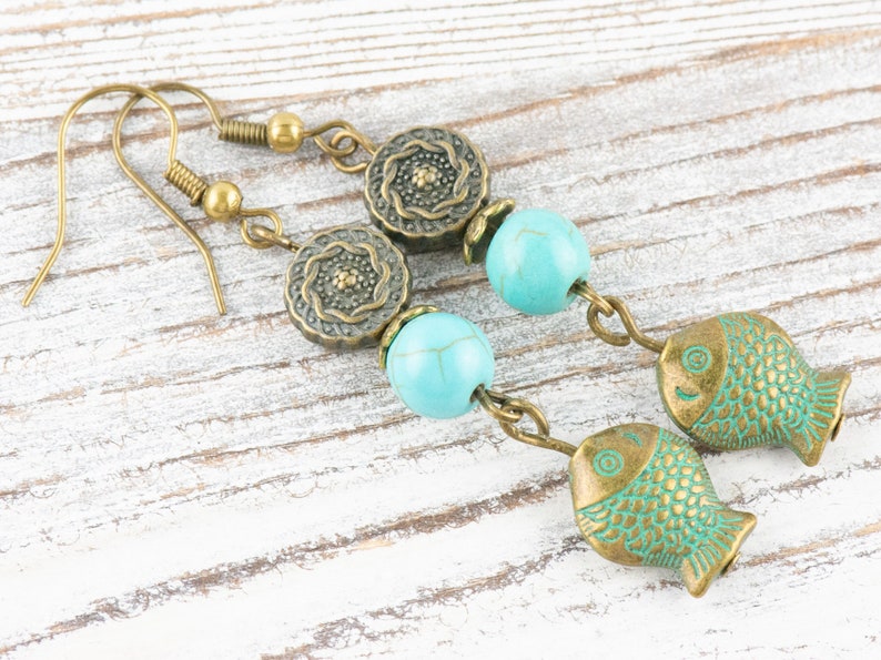 May include: A pair of turquoise and bronze earrings featuring a fish charm, turquoise beads, and ornate bronze accents.