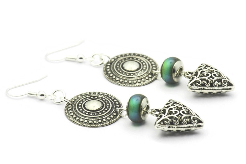 May include: Silver earrings with a round, ornate charm, a green iridescent bead, and a triangular charm with a filigree design.