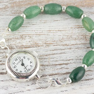 May include: A silver pocket watch with a white face and black hands. The watch is attached to a green jade bead bracelet with silver spacers.