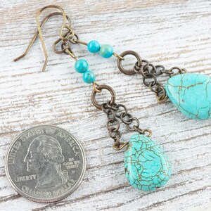 May include: Turquoise and bronze dangle earrings with a teardrop shaped turquoise stone and a chain of bronze beads. The earrings are about the size of a US quarter.