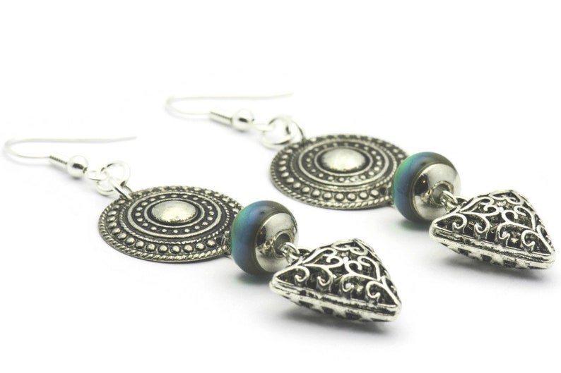 May include: Silver earrings with a round, patterned disc, a blue and green iridescent bead, and a triangular, filigree charm.