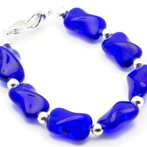Pode incluir: Um bracelete de contas de vidro azul com detalhes prateados. As contas t&ecirc;m uma forma irregular e um acabamento brilhante.