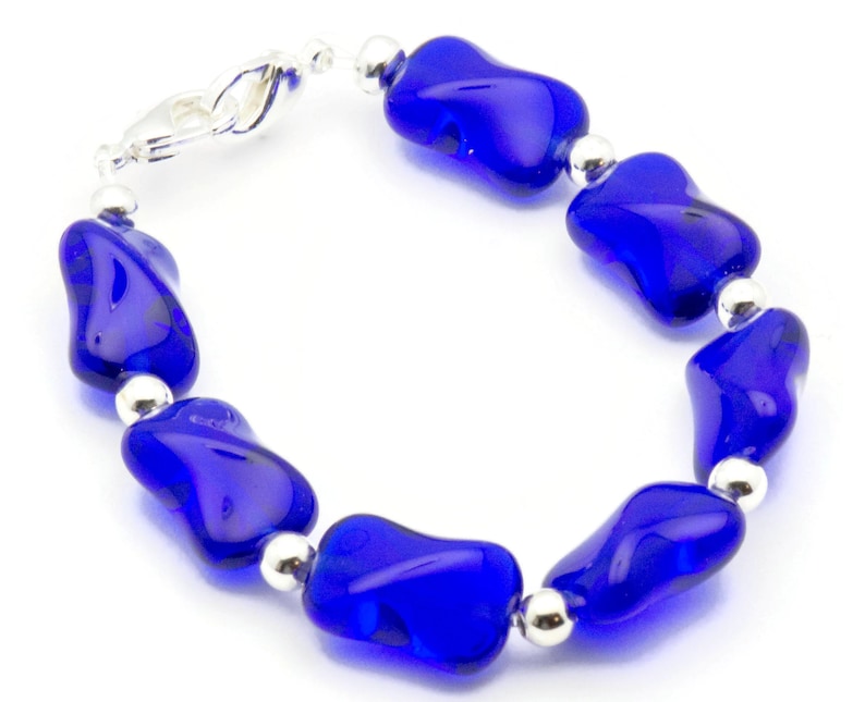 Pode incluir: Um bracelete de contas de vidro azul com detalhes prateados. As contas t&ecirc;m uma forma irregular e um acabamento brilhante.