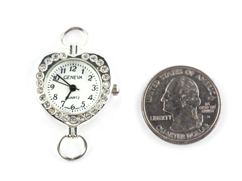 Pu&ograve; includere: Un orologio a forma di cuore argentato con un quadrante bianco e accenti di strass trasparenti. Il quadrante dell'orologio recita "GENEVA QUARTZ" e ha lancette nere. L'orologio &egrave; accanto a un quarto di dollaro americano per il confronto delle dimensioni.