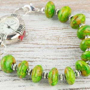 Pode incluir: Um rel&oacute;gio prateado com uma pulseira de contas com padr&atilde;o verde e marrom. O mostrador do rel&oacute;gio tem ponteiros prateados e n&uacute;meros pretos.
