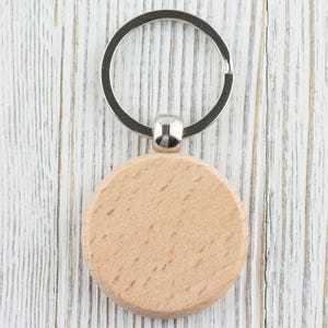 Op de afbeelding: Een ronde houten sleutelhanger met een zilveren metalen ring. De sleutelhanger is leeg en kan worden gepersonaliseerd.