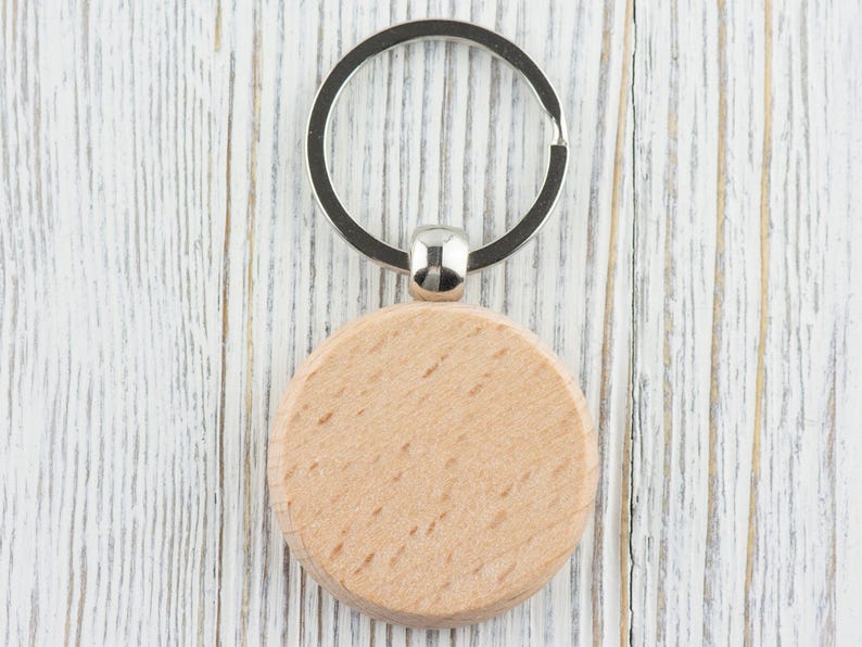 Op de afbeelding: Een ronde houten sleutelhanger met een zilveren metalen ring. De sleutelhanger is leeg en kan worden gepersonaliseerd.