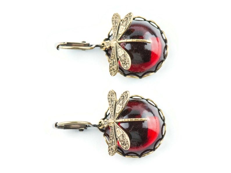 Pode incluir: Um par de brincos com uma pedra de caboch&atilde;o vermelha e preta e um design de lib&eacute;lula dourada.