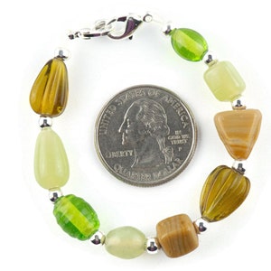 May include: A green, brown and beige beaded bracelet with a silver clasp. The bracelet is about the size of a 25 pence coin.