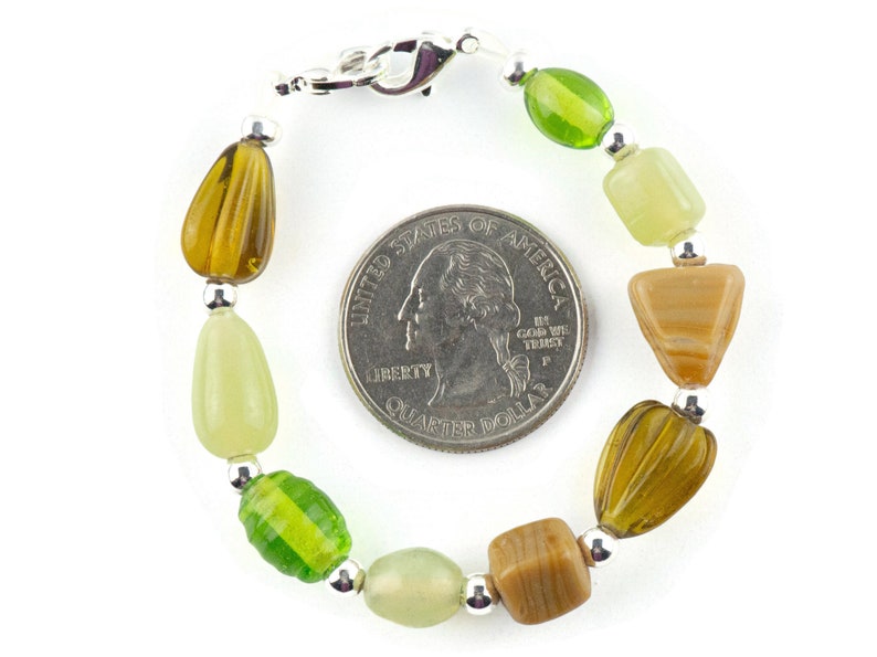 May include: A green, brown and beige beaded bracelet with a silver clasp. The bracelet is about the size of a 25 pence coin.