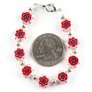 Puede incluir: Un brazalete de plata con cuentas de vidrio blancas y rojas con un dise&ntilde;o de estrella. El brazalete es aproximadamente del tama&ntilde;o de una moneda de 25 centavos de d&oacute;lar estadounidense.