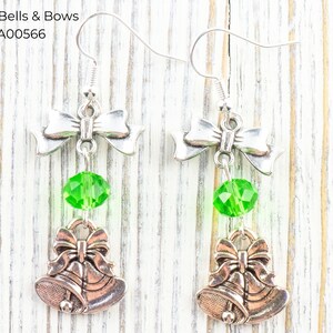 Pode incluir: Brincos prateados com design de la&ccedil;o, uma conta de cristal verde e um berloque de sino. Os brincos t&ecirc;m fecho de gancho. O texto "Green Bells & Bows" e "EA00566" s&atilde;o vis&iacute;veis na imagem.