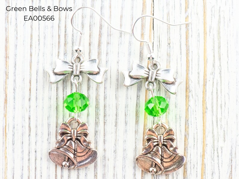 Pode incluir: Brincos prateados com design de la&ccedil;o, uma conta de cristal verde e um berloque de sino. Os brincos t&ecirc;m fecho de gancho. O texto "Green Bells & Bows" e "EA00566" s&atilde;o vis&iacute;veis na imagem.