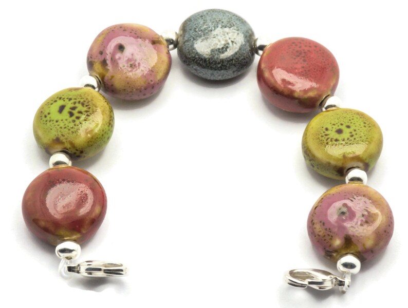 May include: A bracelet made of ceramic beads in shades of green, red, and grey. The beads are speckled with different colours and have a glossy finish. The bracelet is secured with a silver clasp.