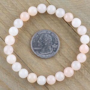 Op de afbeelding: Een armband gemaakt van witte en lichtroze kralen. De armband is ongeveer zo groot als een kwartje.