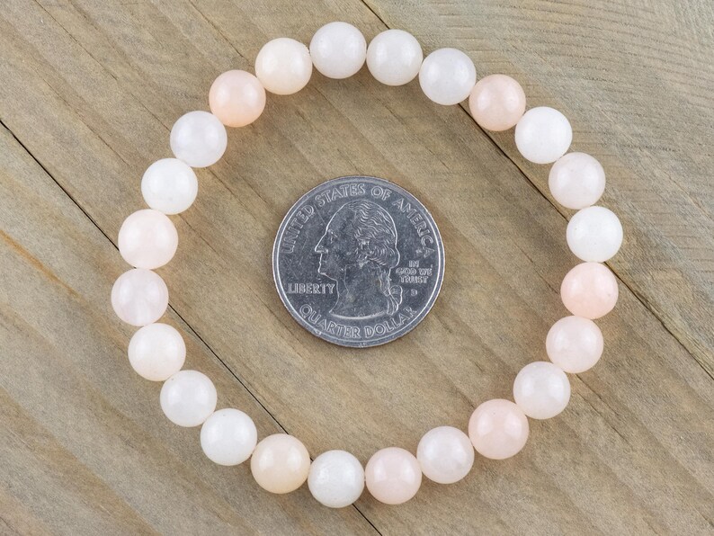 Op de afbeelding: Een armband gemaakt van witte en lichtroze kralen. De armband is ongeveer zo groot als een kwartje.