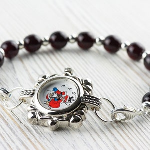 May include: A silver watch with a Santa Claus design on the face, attached to a bracelet made of dark red beads.