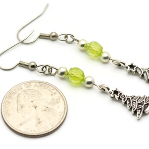 May include: Silver dangle earrings with green and white beads and a silver Christmas tree charm. The earrings are about the size of a quarter.