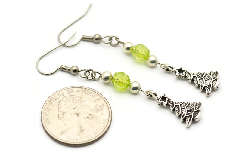 May include: Silver dangle earrings with green and white beads and a silver Christmas tree charm. The earrings are about the size of a quarter.