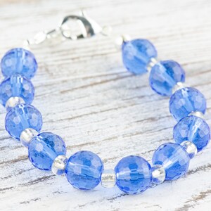 Pu&ograve; includere: Un braccialetto con perline di cristallo blu con una chiusura argentata. Le perline sono sfaccettate e hanno un colore blu chiaro.