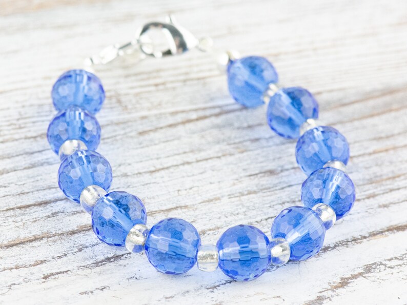 Pu&ograve; includere: Un braccialetto con perline di cristallo blu con una chiusura argentata. Le perline sono sfaccettate e hanno un colore blu chiaro.