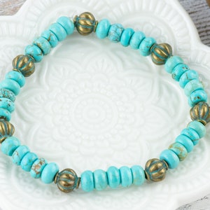May include: A turquoise and brass beaded bracelet. The bracelet is made with small, round turquoise beads and larger, round brass beads with a decorative design.