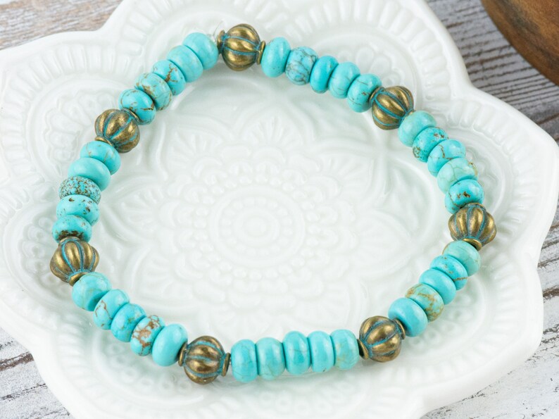 May include: A turquoise and brass beaded bracelet. The bracelet is made with small, round turquoise beads and larger, round brass beads with a decorative design.