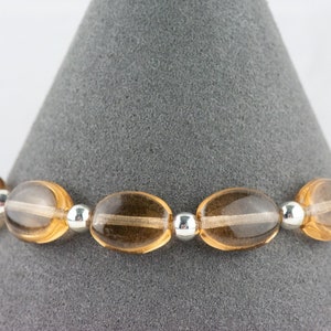 May include: A brown gemstone bracelet with silver beads. The bracelet is made of oval-shaped stones and is displayed on a gray background.