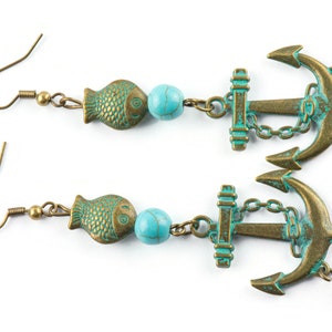 Puede incluir: Un par de pendientes de color turquesa y bronce con un dije de ancla, un dije de pez y una cuenta turquesa.