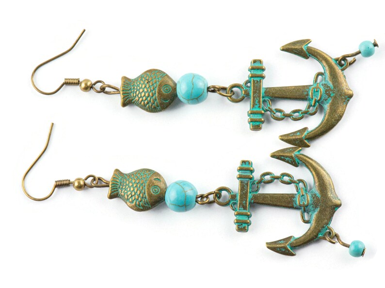 Puede incluir: Un par de pendientes de color turquesa y bronce con un dije de ancla, un dije de pez y una cuenta turquesa.