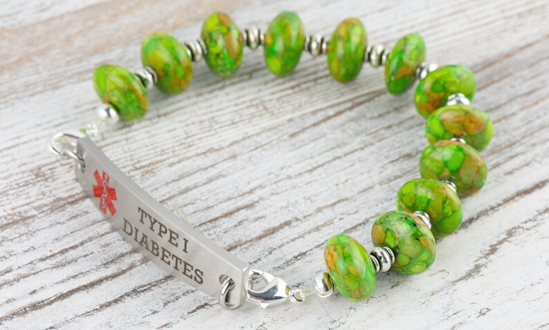 Pode incluir: Um bracelete de alerta m&eacute;dica verde e prateado com as palavras "Type I Diabetes" gravadas em uma placa de metal. O bracelete tem um s&iacute;mbolo m&eacute;dico e &eacute; feito com contas de pedra verde.