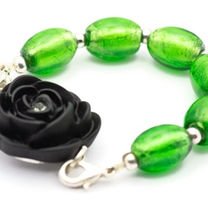 May include: A black fabric rose charm bracelet with green glass beads. The bracelet has a silver clasp.